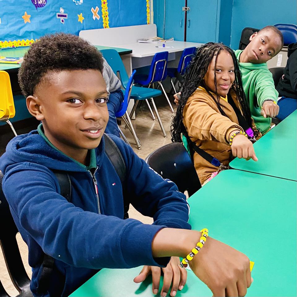 A boy holding out his wrist to show a bead bracelet.